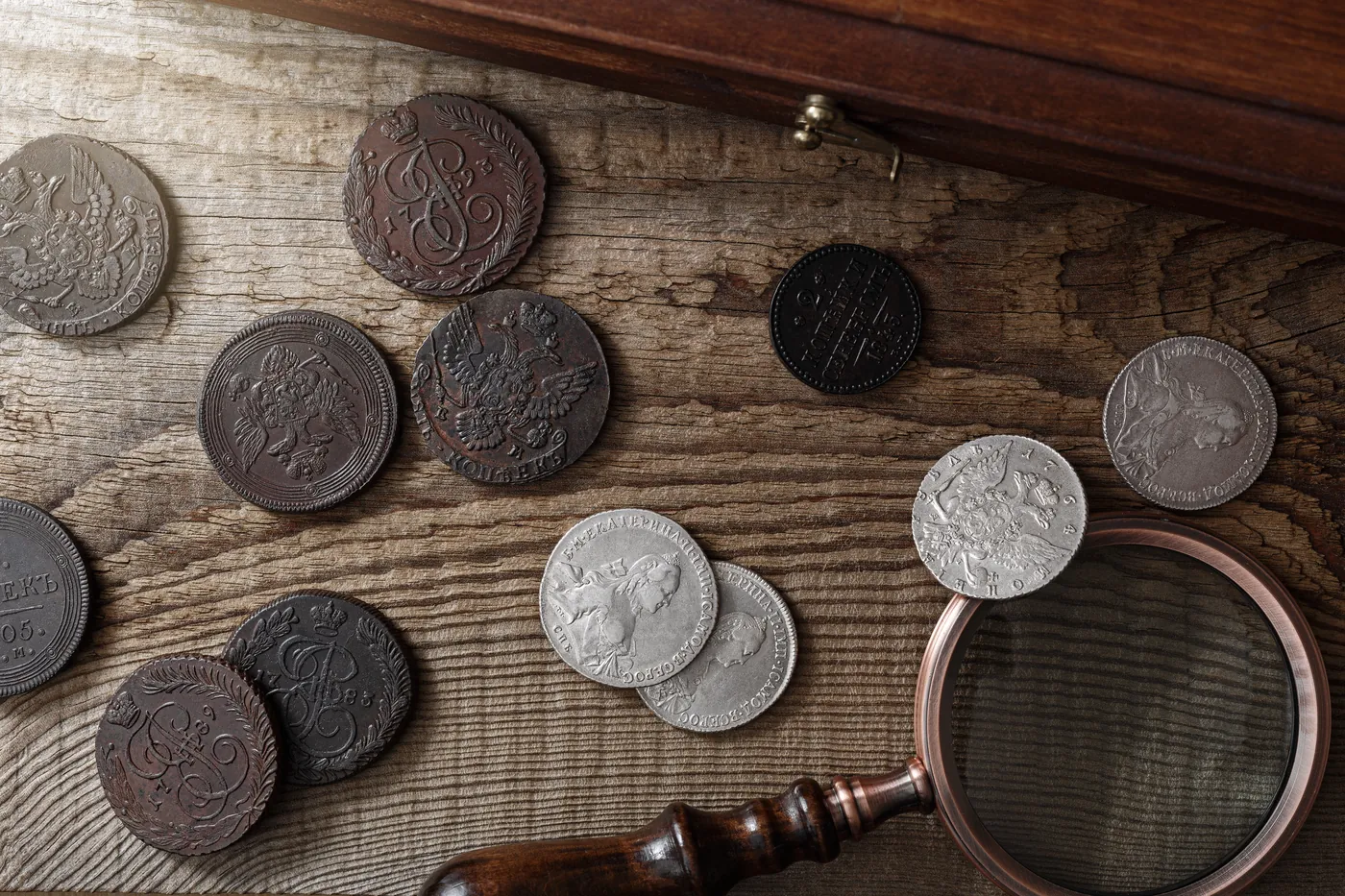 Old collectible coins laid out on a wooden table with a magnifying glass